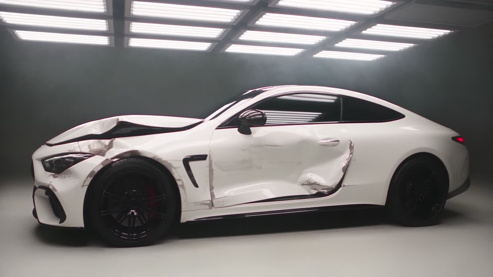 The white coupe before repair: crushed hood and fender, the driver’s door caved in and scraped